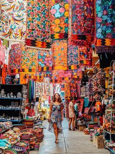 a woman walking through an open market with lots of colorful items hanging from the ceiling