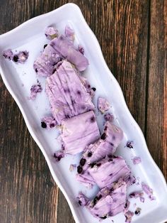 a white plate topped with blueberry ice cream on top of a wooden table next to a spoon