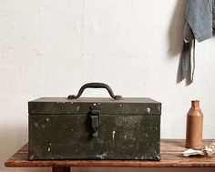 an old metal box sitting on top of a wooden table next to a vase and bottle