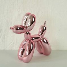 a shiny pink balloon dog sitting on top of a table next to a white wall