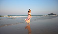 a woman is walking on the beach with her dress blowing in the wind