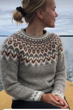 a woman sitting on the edge of a boat looking out at the water while wearing a sweater