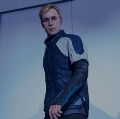 a man with blonde hair wearing a blue and grey leather jacket standing in front of a white wall