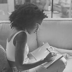 a black and white photo of a woman sitting on a couch holding a binder