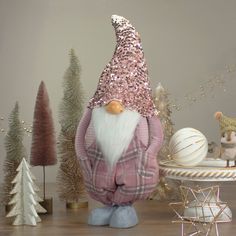 a gnome statue sitting in front of some christmas trees and ornaments on a wooden table