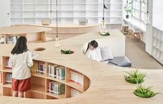 two people standing in front of bookshelves with shelves full of books and plants