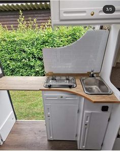 an rv kitchen with sink, stove and refrigerator in the back ground next to bushes