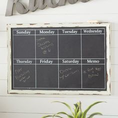 a blackboard with days and months on it in front of a potted plant