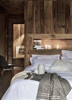 a bed with white linens and pillows in a rustic style bedroom, surrounded by wood paneled walls