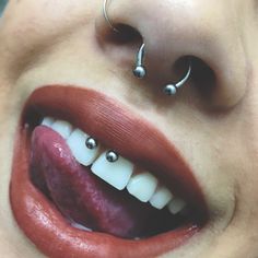 a close up of a person with piercings on their nose and tongue, smiling at the camera