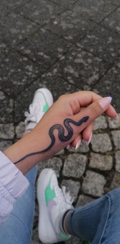 a woman's hand with a snake tattoo on her left wrist and white sneakers