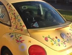 the back end of a yellow car with flowers painted on it's side window