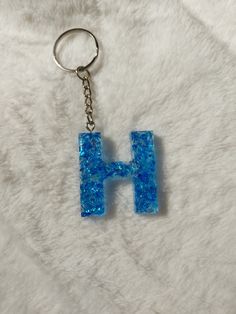 the letter h is made out of glittery blue beads and sits on a white fur surface