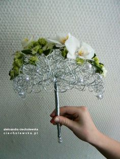 a hand holding a wire umbrella with flowers on the top and pearls attached to it