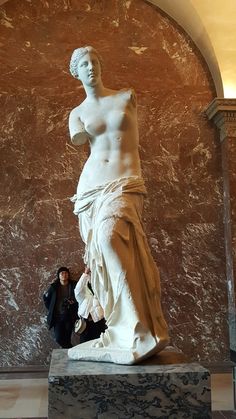 a woman standing next to a statue in a room with marble walls and flooring