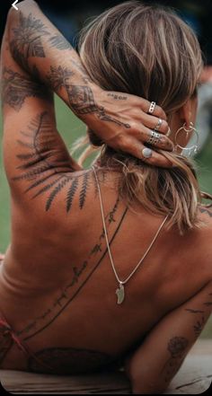 a woman with tattoos on her back sitting down and holding her hands behind her head