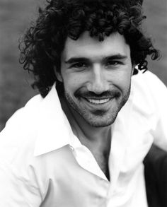 a black and white photo of a man with long curly hair smiling at the camera