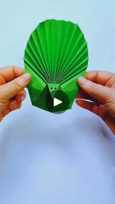 two hands holding up a green paper fan with the video below it that reads, how to make an origami fan