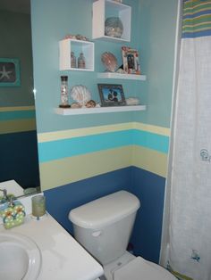 a white toilet sitting next to a sink in a bathroom under a shelf filled with pictures