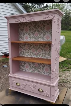 an old dresser is painted pink and has floral wallpaper on the back, along with wooden shelves