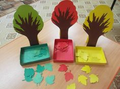 three trees cut out of paper sitting on top of a table next to a tray with leaves