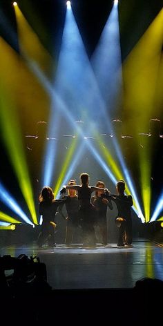 a group of people standing on top of a stage surrounded by bright colored spotlights