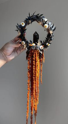 a person holding up a piece of art made out of flowers and leaves with chains attached to it