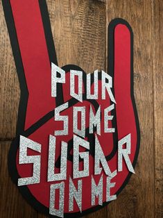 a red and black sign that says pour some sugar in me on top of a wooden floor