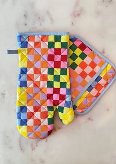 an oven mitt and pot holder made out of colored squares on a marble surface