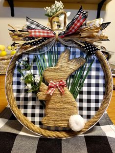 an easter decoration made out of straw and grass with a bunny on the front, sitting on a checkered table cloth