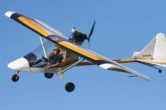 a man is sitting in the cockpit of a small plane flying through the air with his feet on the ground