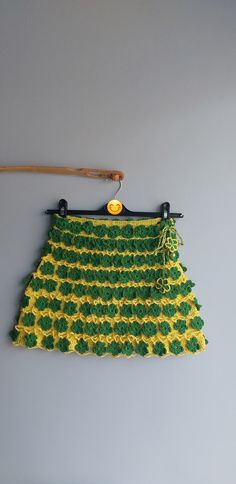 a green and yellow crocheted skirt hanging on a wall with a wooden hanger