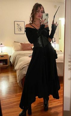 a woman in a black dress taking a selfie with her cell phone while standing on a wooden floor