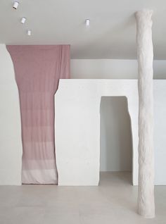 an empty room with white walls and pink drapes hanging from the ceiling in front of two columns