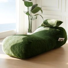 a green bean bag chair sitting on top of a wooden floor next to a plant