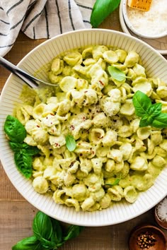 a white bowl filled with pasta and pesto on top of a wooden table next to bowls