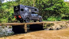 an off road vehicle is parked on a bridge over a river with trees in the background