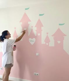 a woman is painting a pink castle on the wall