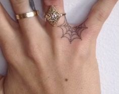 a woman's hand with a ring and spider web tattoo on the middle finger