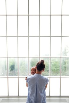 a woman holding a baby in her arms while standing next to a large glass window