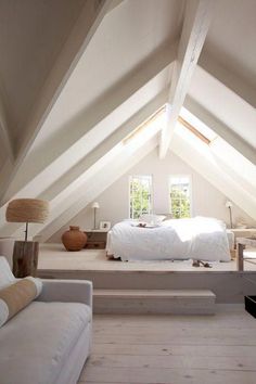 an attic bedroom with white bedding and furniture on the floor, along with two couches