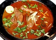 a black bowl filled with meat and garnish on top of a white table