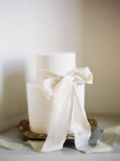 a white wedding cake with a bow on it's top sitting on a plate