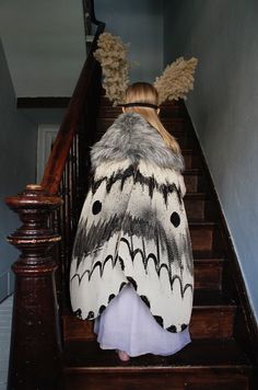 a woman is walking down the stairs with a large moth on her coat over her shoulders