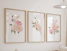 three floral paintings hang on the wall above a couch in a living room with white walls