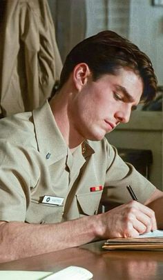 a man in uniform writing on a piece of paper at a desk with a pen