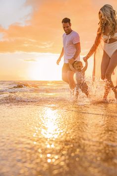 a man, woman and child are playing in the water at sunset on the beach