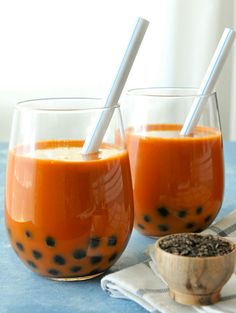 two glasses filled with orange juice on top of a blue table next to a spoon