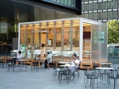 people are sitting at tables outside in front of a building with glass doors and windows