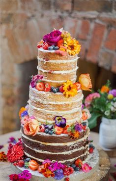 a multi layer cake with flowers on top sitting on a table next to a fireplace